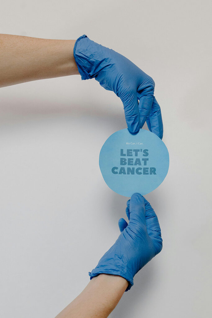 Two hands wearing blue gloves hold a round, blue sign that reads "Let's Beat Cancer. - Blue Ridge Medical Center